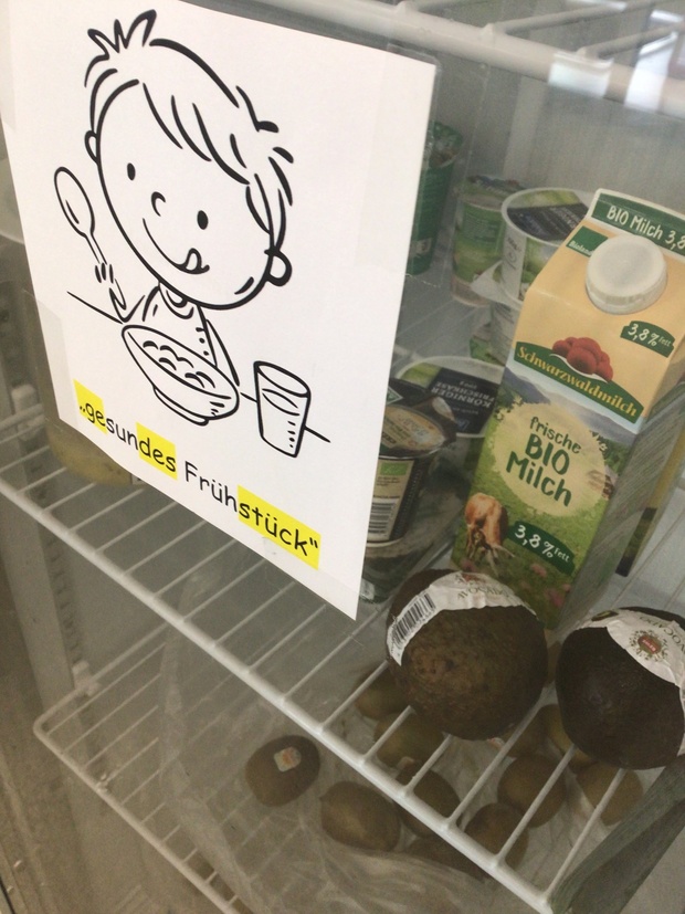 gefüllter Kühlschrank von außen: durch die Glasscheibe sieht man Bioprodukte wie Milch, Joghurt, Quark und auch Avocado und Kiwis. An der Scheibe hängt ein Zettel auf dem
