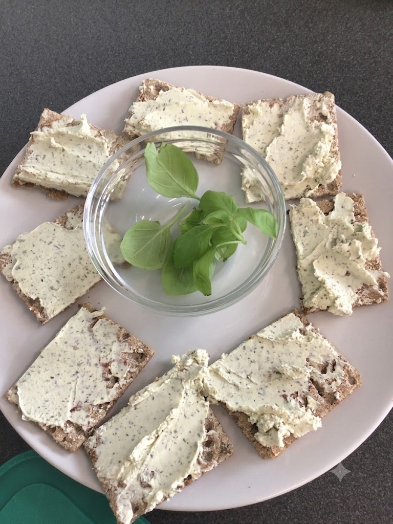 Knäckebrot mit Frischkäse in einem Kreis auf einem Teller angerichtet, in der Mitte Basilikumblätter in einer Schale, © Nora Leiner